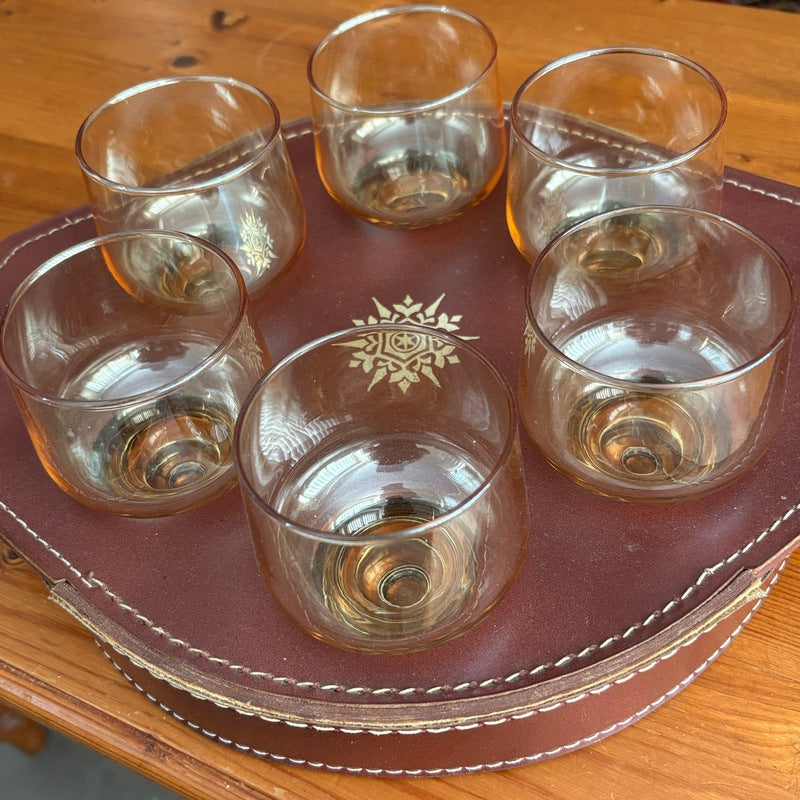 Six Crown Crystal Regis gold lustre lowball glasses arranged in a brown leather tray