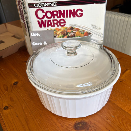 A white Corning ribbed casserole dish with a clear glass lid, shown on a wooden table with the Corning product box in the background.